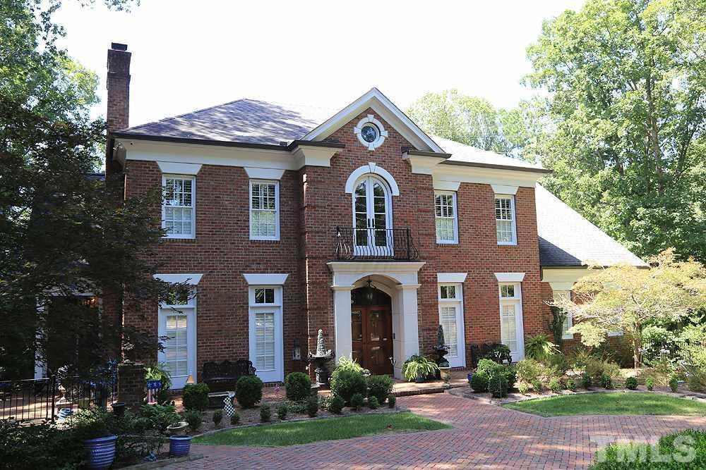 A two-story brick home with white trim, stone front entrance, manicured landscaping, surrounded by trees